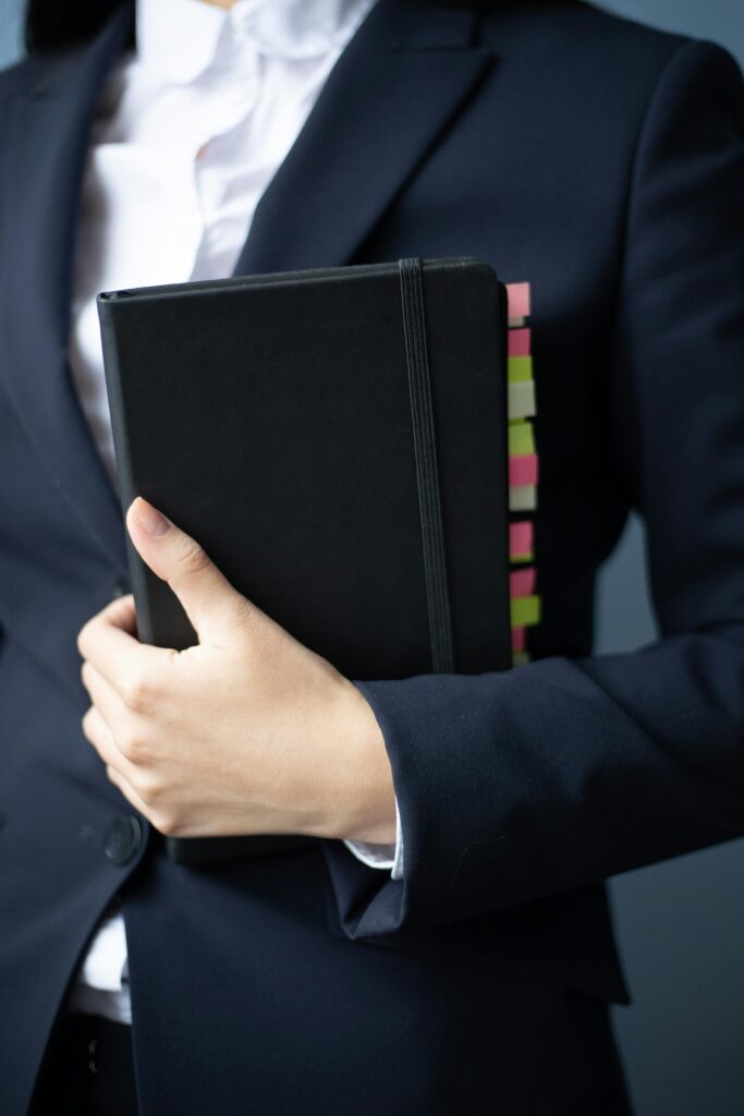 pexels-photo-6077981-6077981 A businesswoman in a suit holds a planner with colorful tabs in an office setting.
